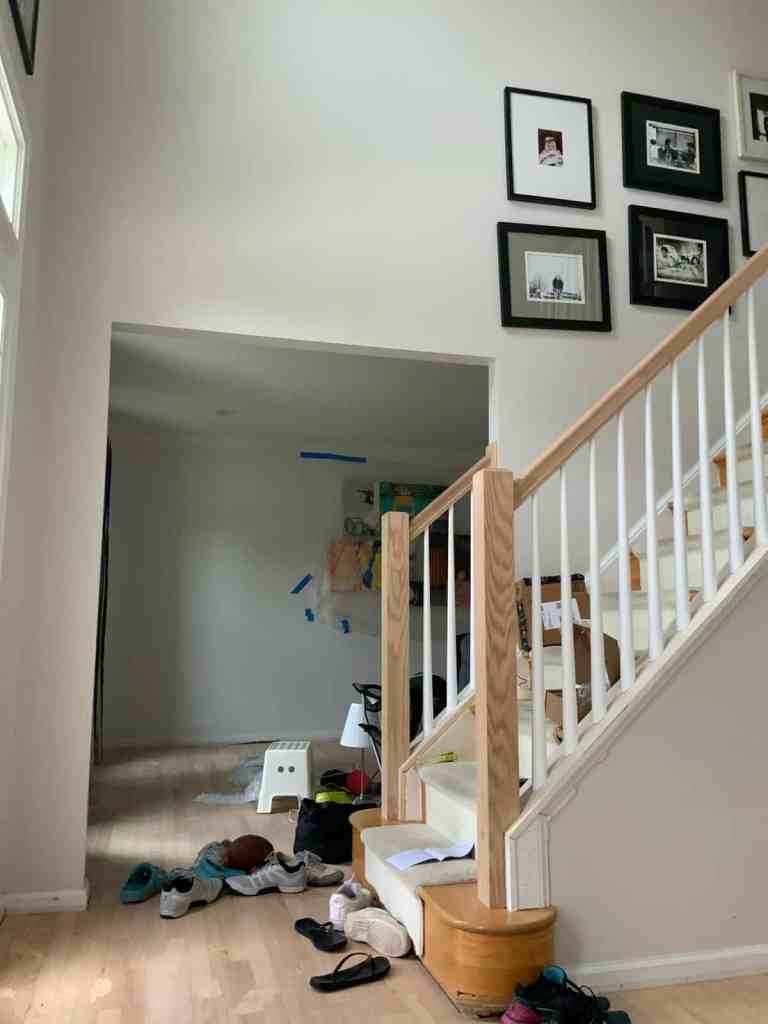 Bright room featuring staircase, framed photos, and casual shoe clutter on hardwood floor.