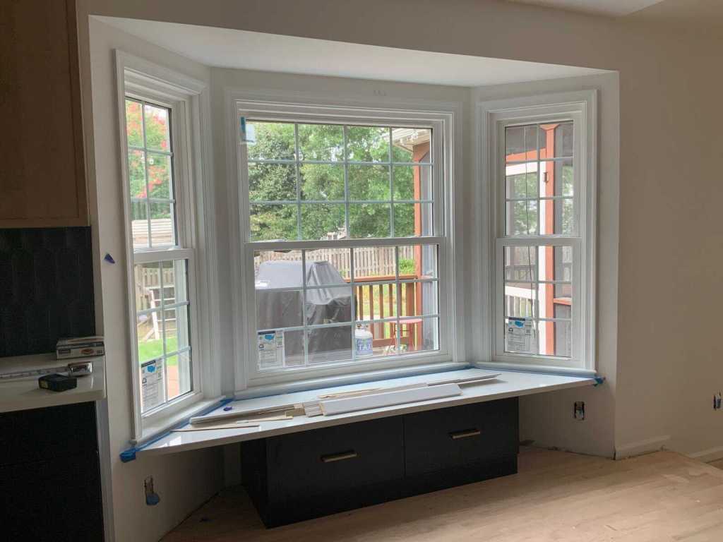 Bright bay window with white trim installed in modern kitchen, offering natural light and a view of the backyard.