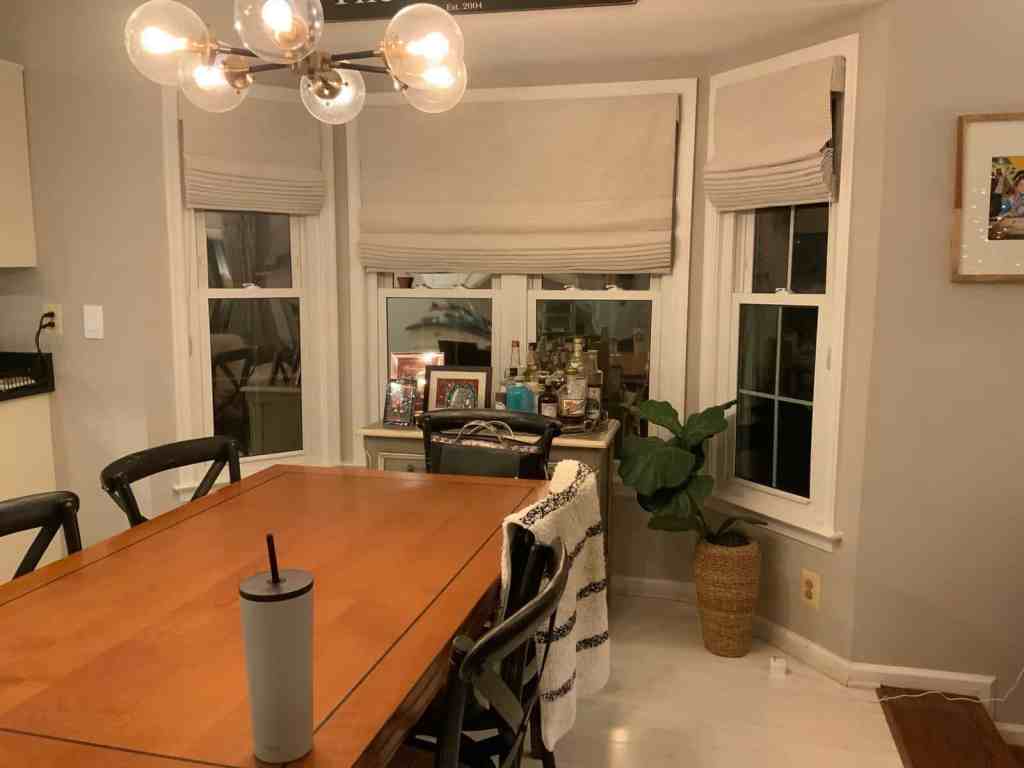 Elegant dining space with window treatments, potted plant, and bar cart.