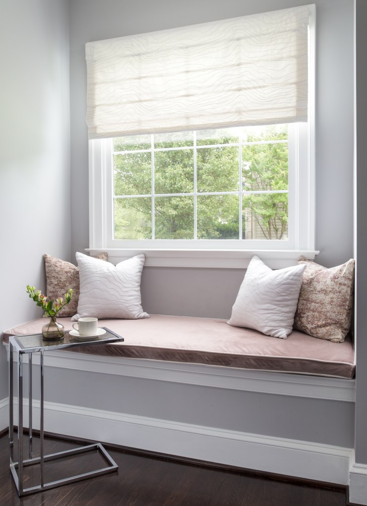 Bright reading nook with soft cushions, decorative pillows, and natural light from large window.