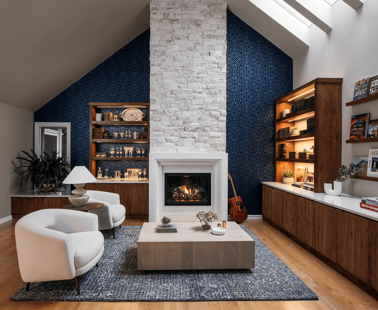 Living room with a cathedral ceiling, stacked stone fireplace, navy velvet walls, walnut built-ins, and a guitar by the hearth.